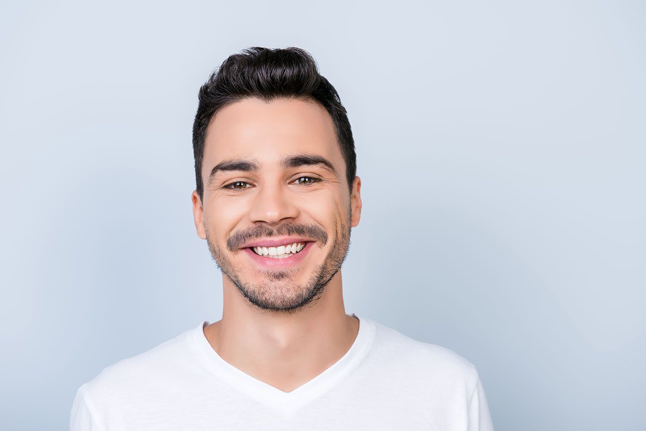 young man with a beautiful smile in a white shirt on a gray retainer invisalign dentist in Frederick Maryland